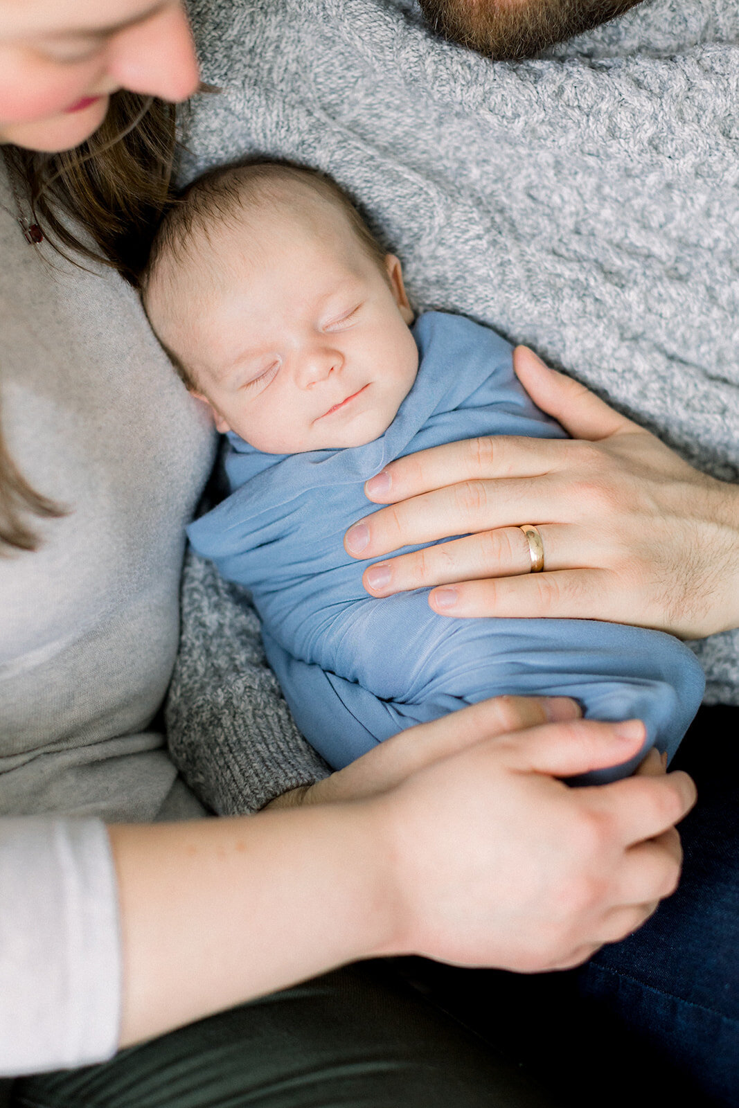 Parents hands on a newborn baby swaddled in blue cloth
