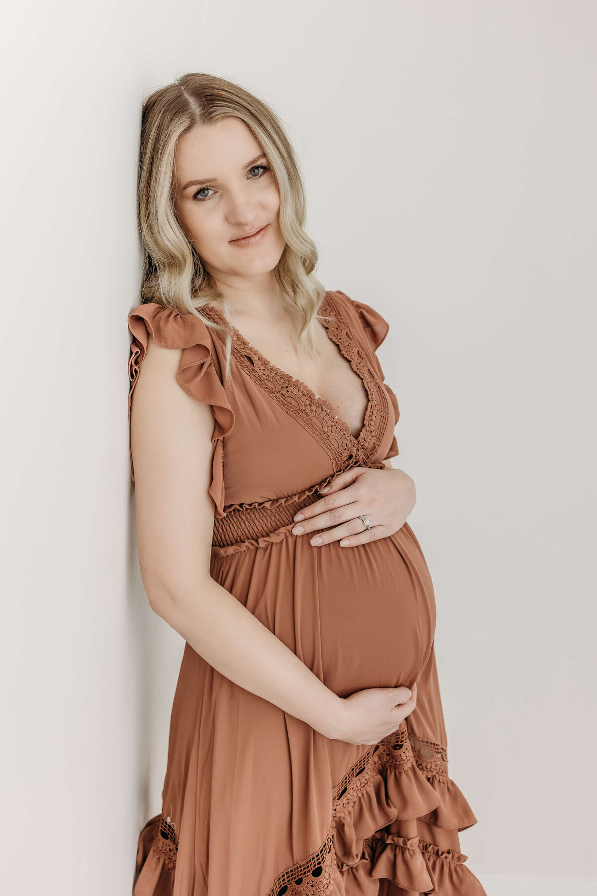 Smiling blonde pregnant mom leaning up against a wall looking at camera