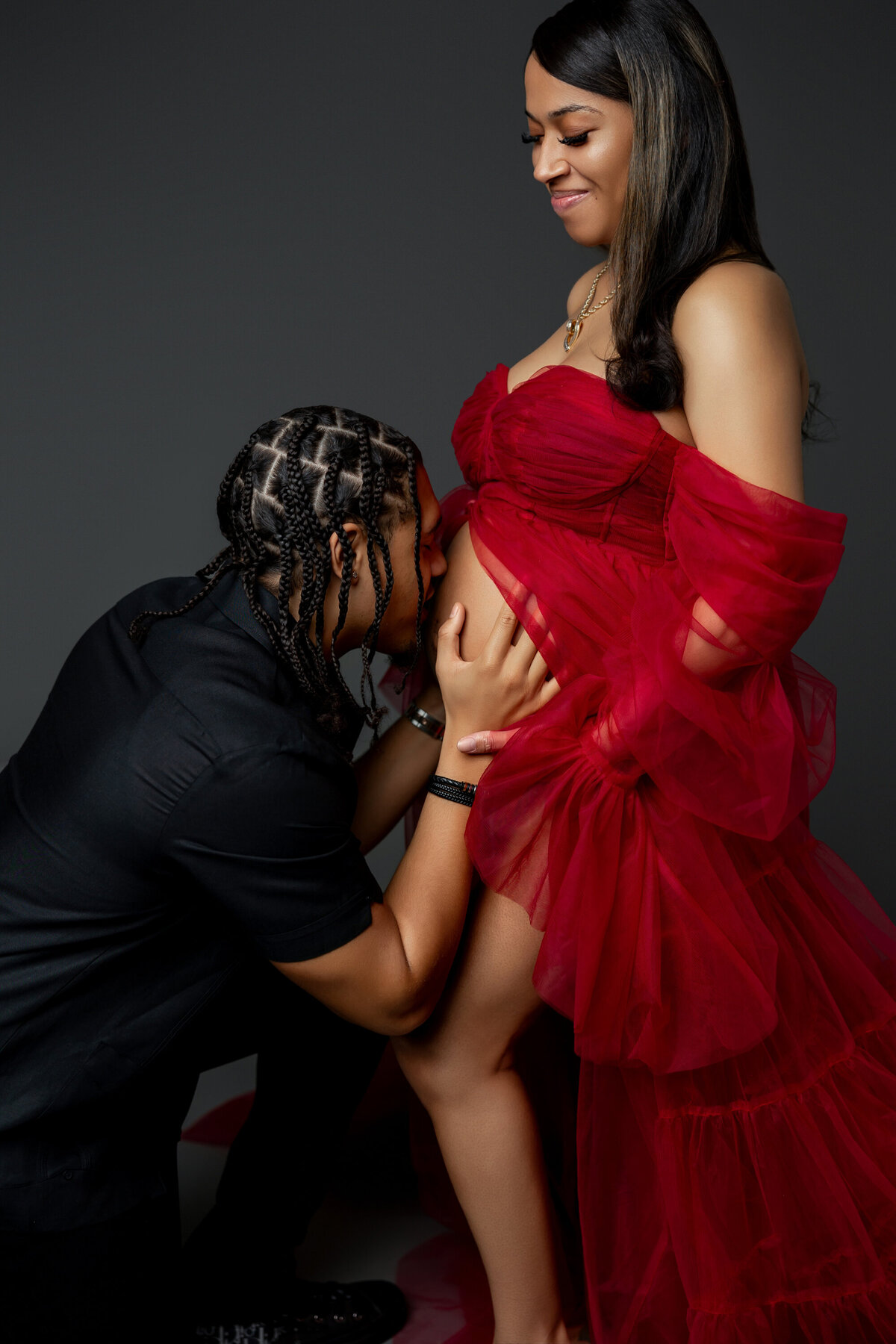 Mama-to-be in a red dress, her husband lovingly kisses her belly in a close-up shot, capturing a beautiful moment of connection. Captured by Inland Empire photographer Kaitlyn Dawn Photography.