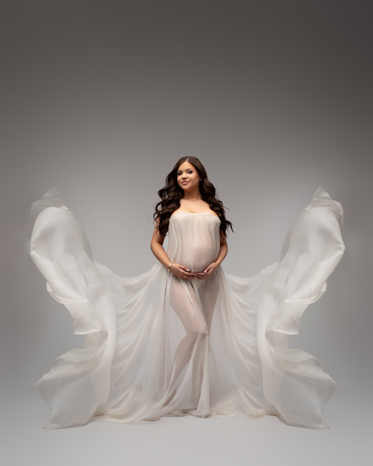 Pregnant woman wearing flowing white fabric looks like angel wings on white backdrop