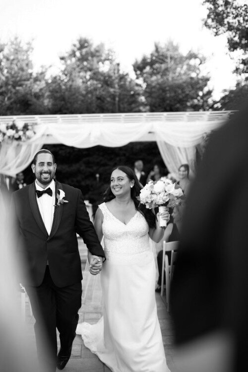 Black and white photograph of a joyful couple walking down the aisle on their wedding day.