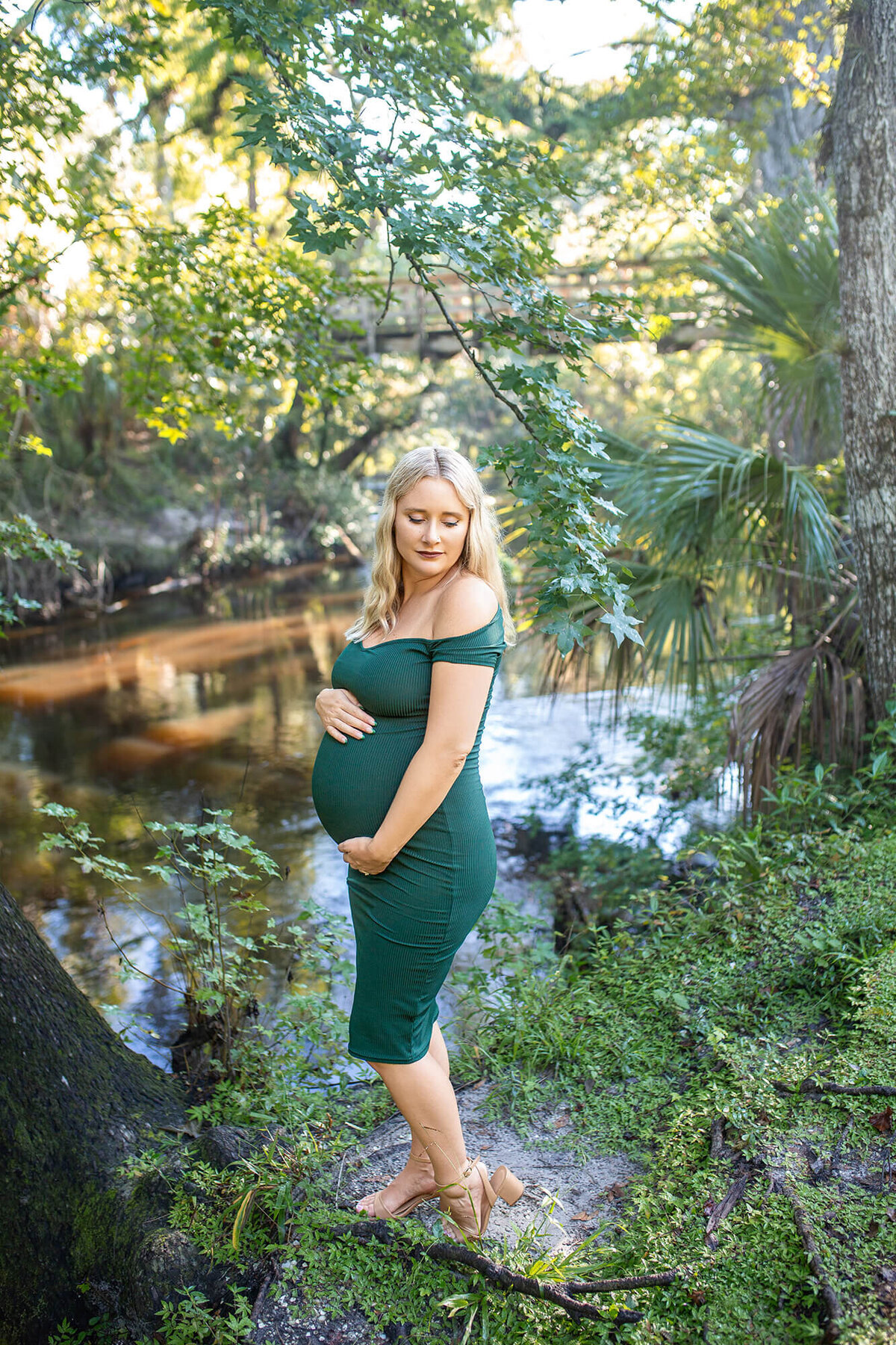 Blond mother in green dress holding belly looking over her sholder