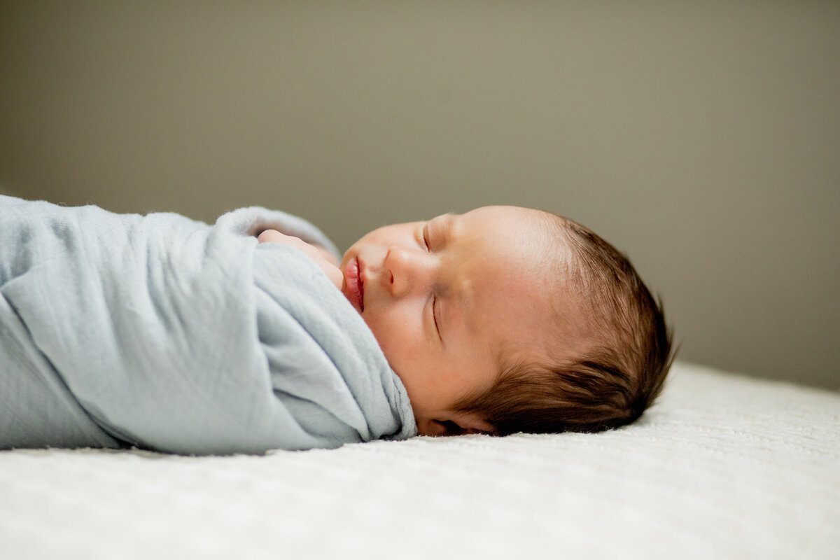 sleeping newborn baby boy who is swaddled in blye