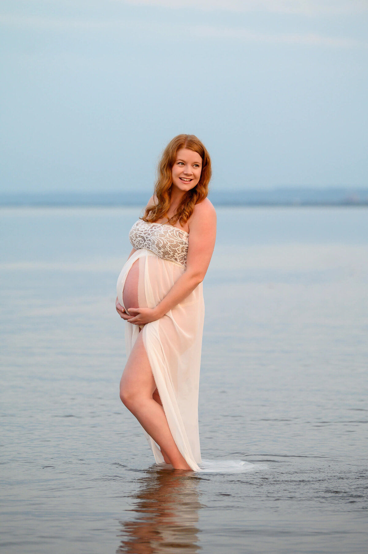 pregnant woman wearing a white maternity dress in the water for her beach maternity photography session in Burlington, Ontario