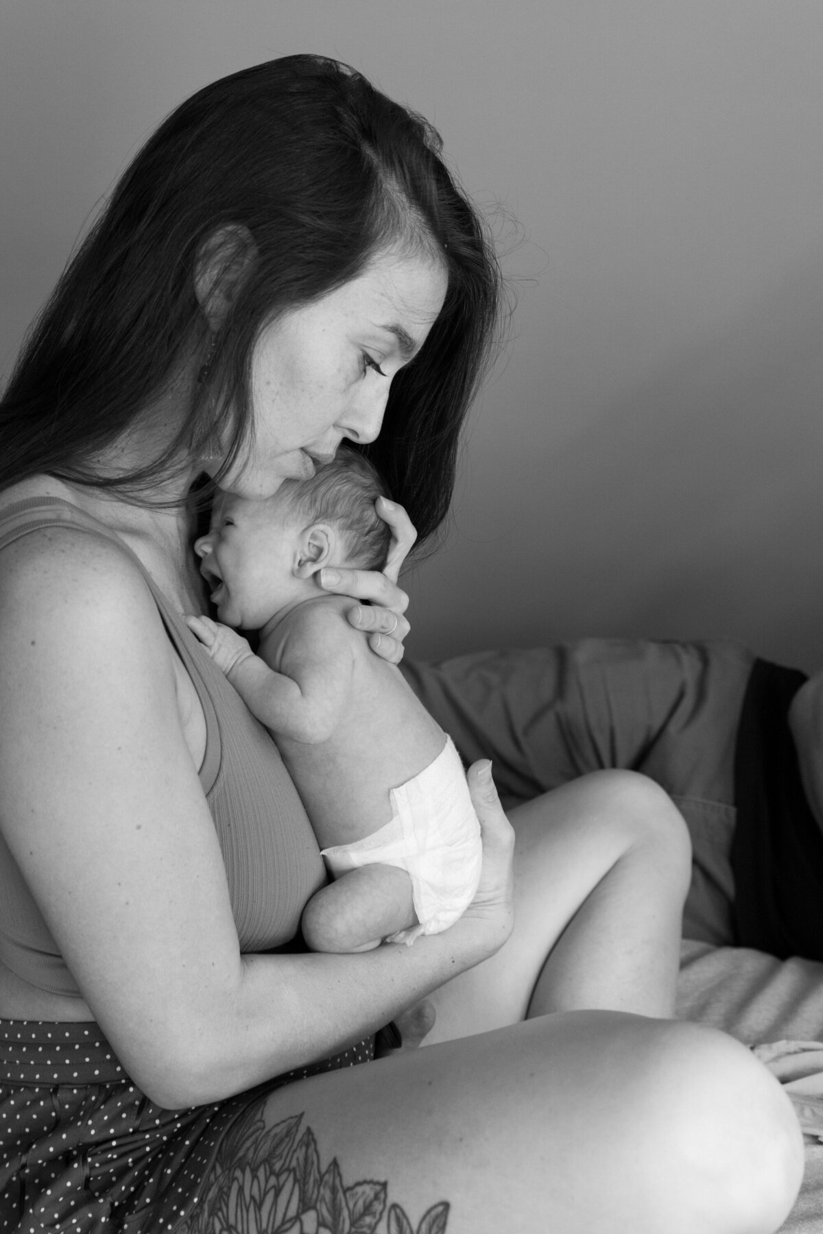 Black and white image of a mother holding her newborn in a diaper. Classic family photography capturing the early days.