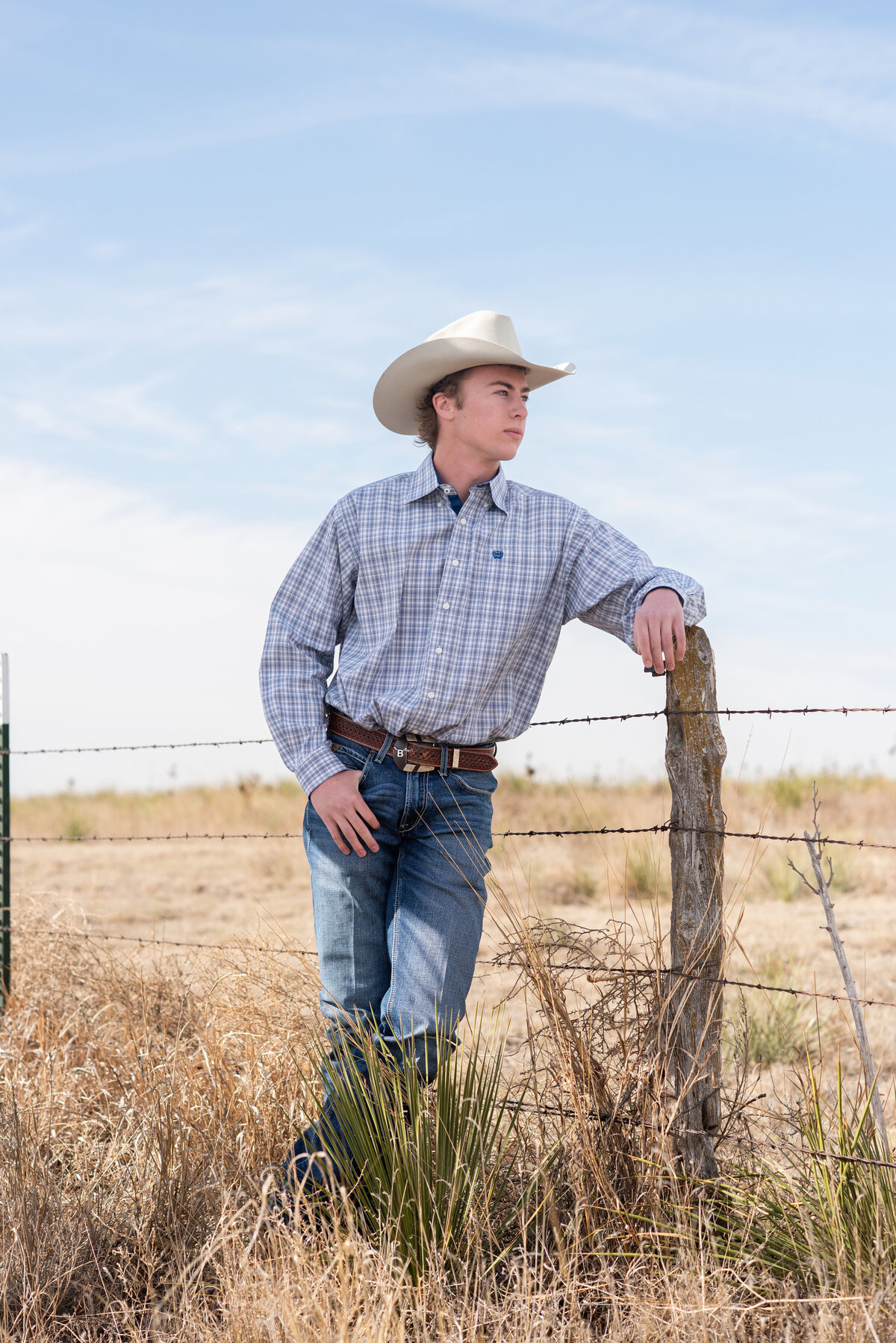 Casual photo of high school senior leaning on post in outdoor country scenery