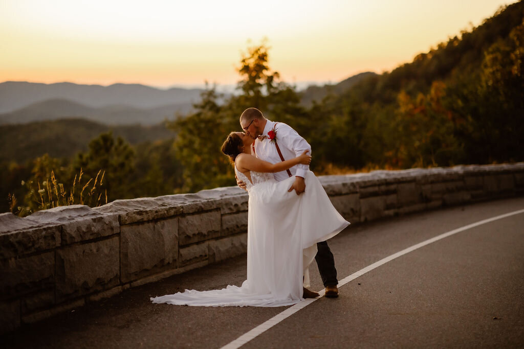 Gatlinburg photographer captures couples eloping to Gatlinburg in the Foothills Parkway with groooom dipping his bride backwards as she holds her bouquet over her head with the SMoky Mountains as the backdrop 