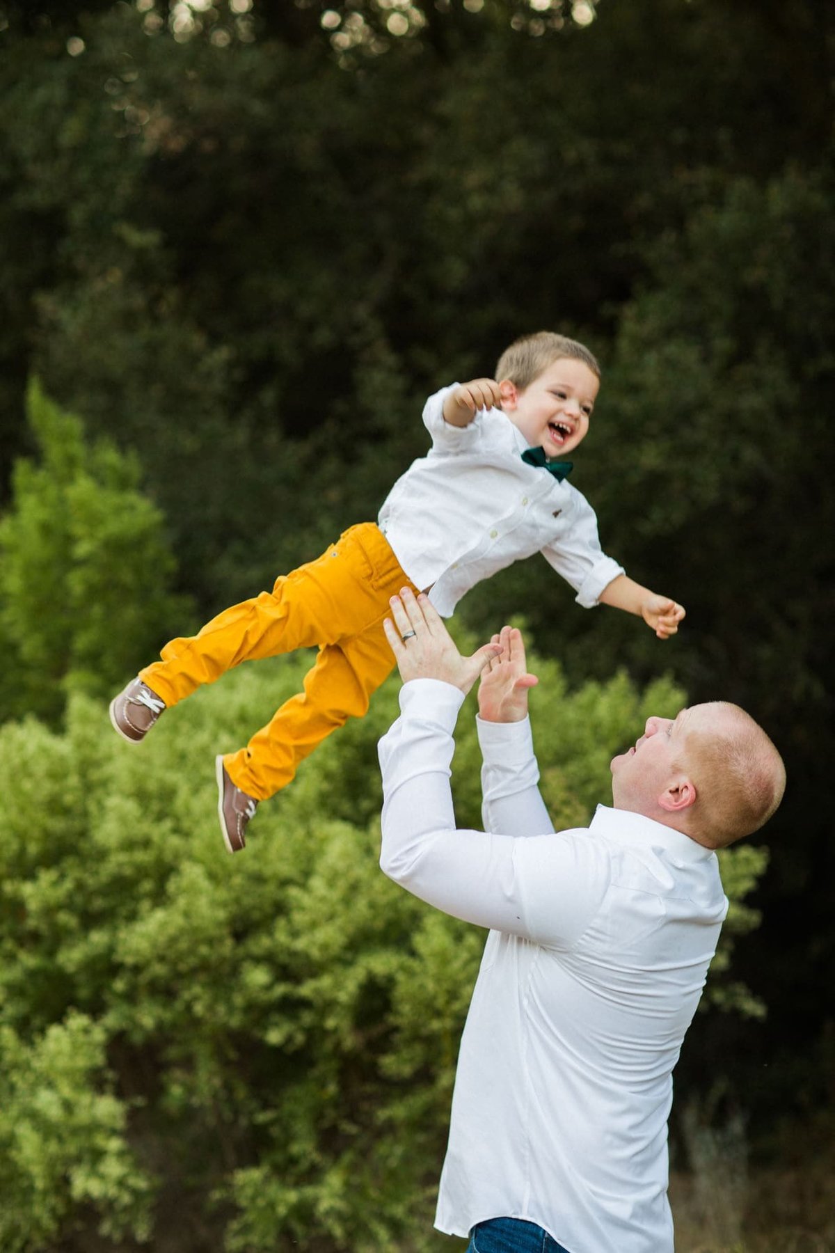 Father tosses his young son in the air before catching him as the little boy gives a big smile