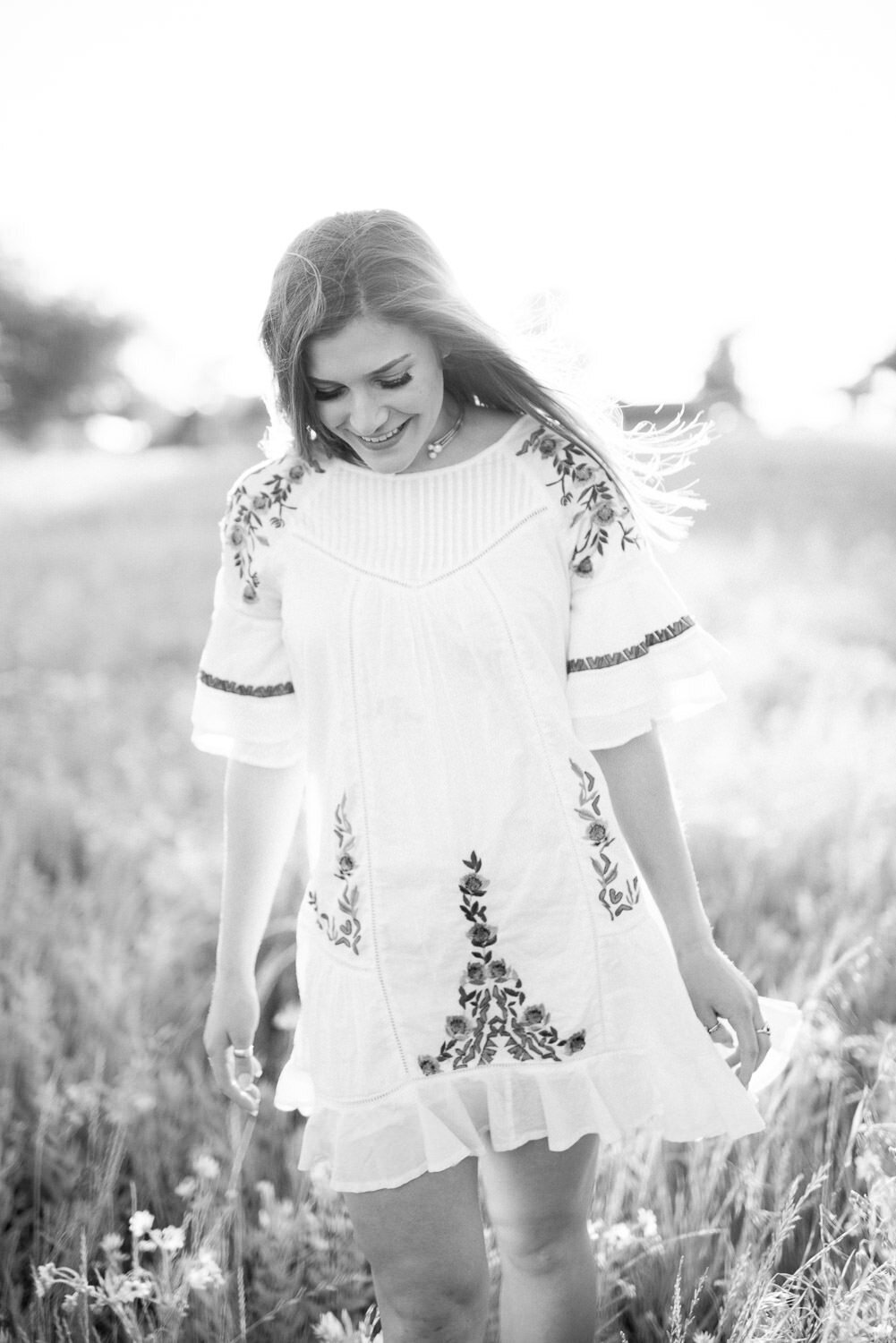 Senior portrait of a girl walking through a field in a flowing floral sundress.


