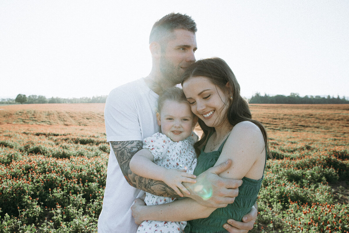 Family of three huddles together while smiling during sunset in Oregon. 