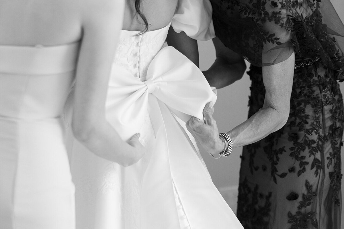 girls helping fix the back of the bride's dress, which has a bow.