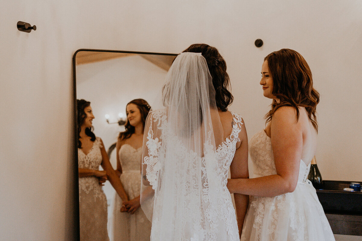 two brides looking in the mirror together in their wedding dresses