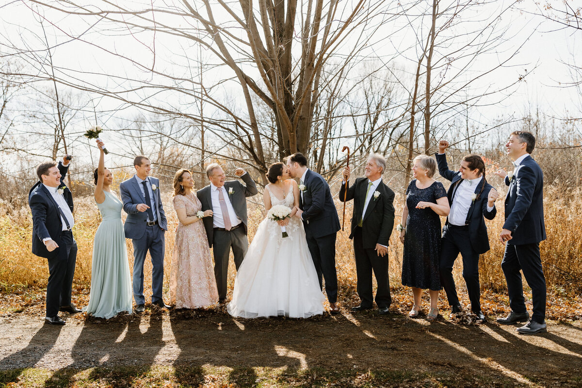 Bride and groom sharing a kiss in the family group photo, outside the wedding venue