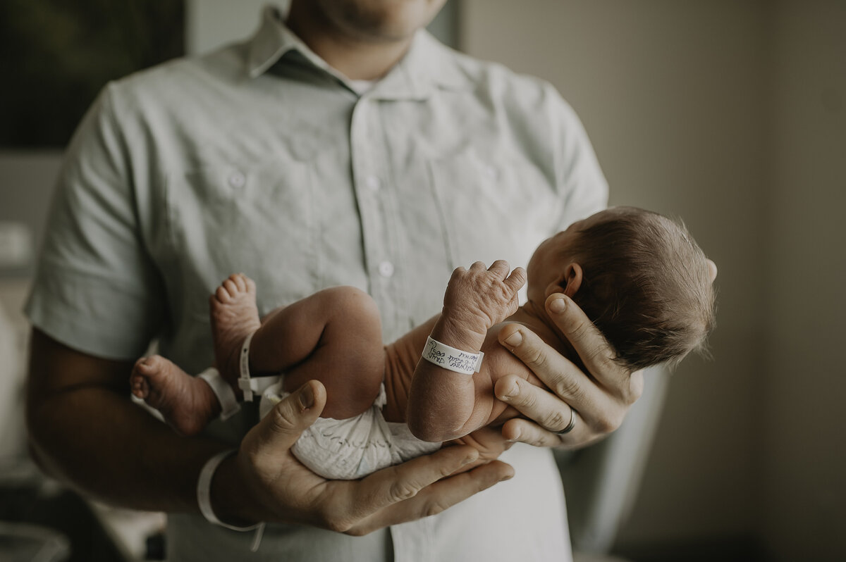 Verona B Photography captures a dad holding his squishy adorable newborn baby. Baby looks so small in daddy’s hands – Akron General Hospital session.