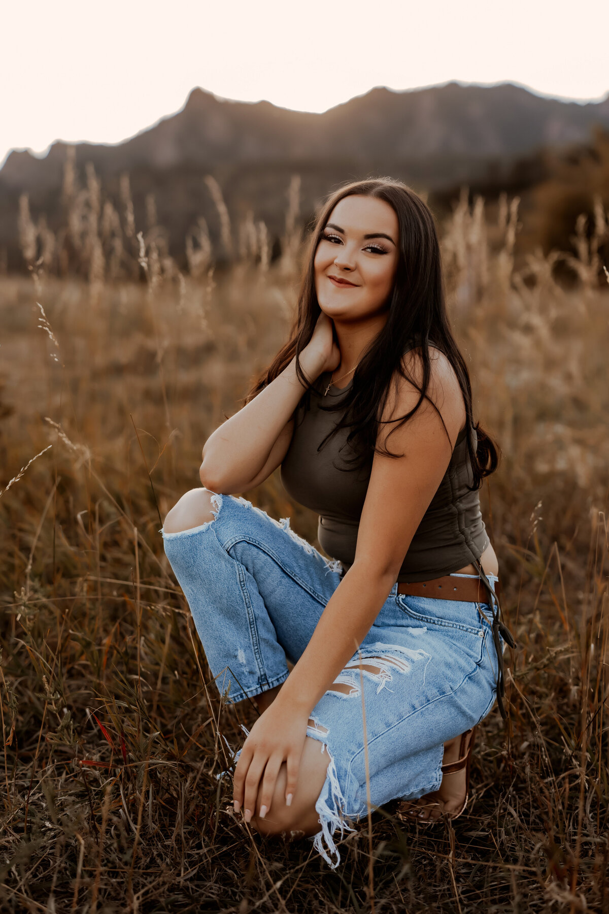 Senior girl kneeling in Boulder, Colorado for her senior photos in a golden grassy field