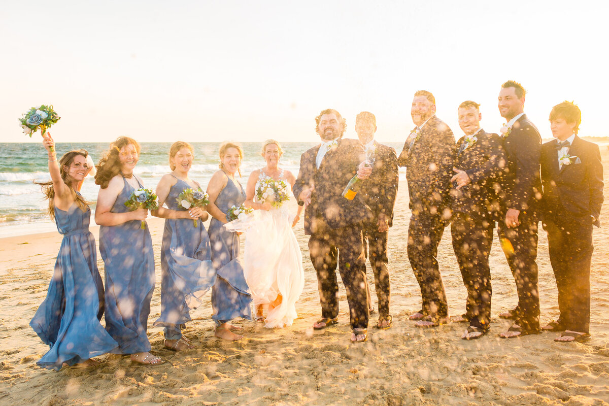 Wedding party cheers as they pop champagne on the beach.