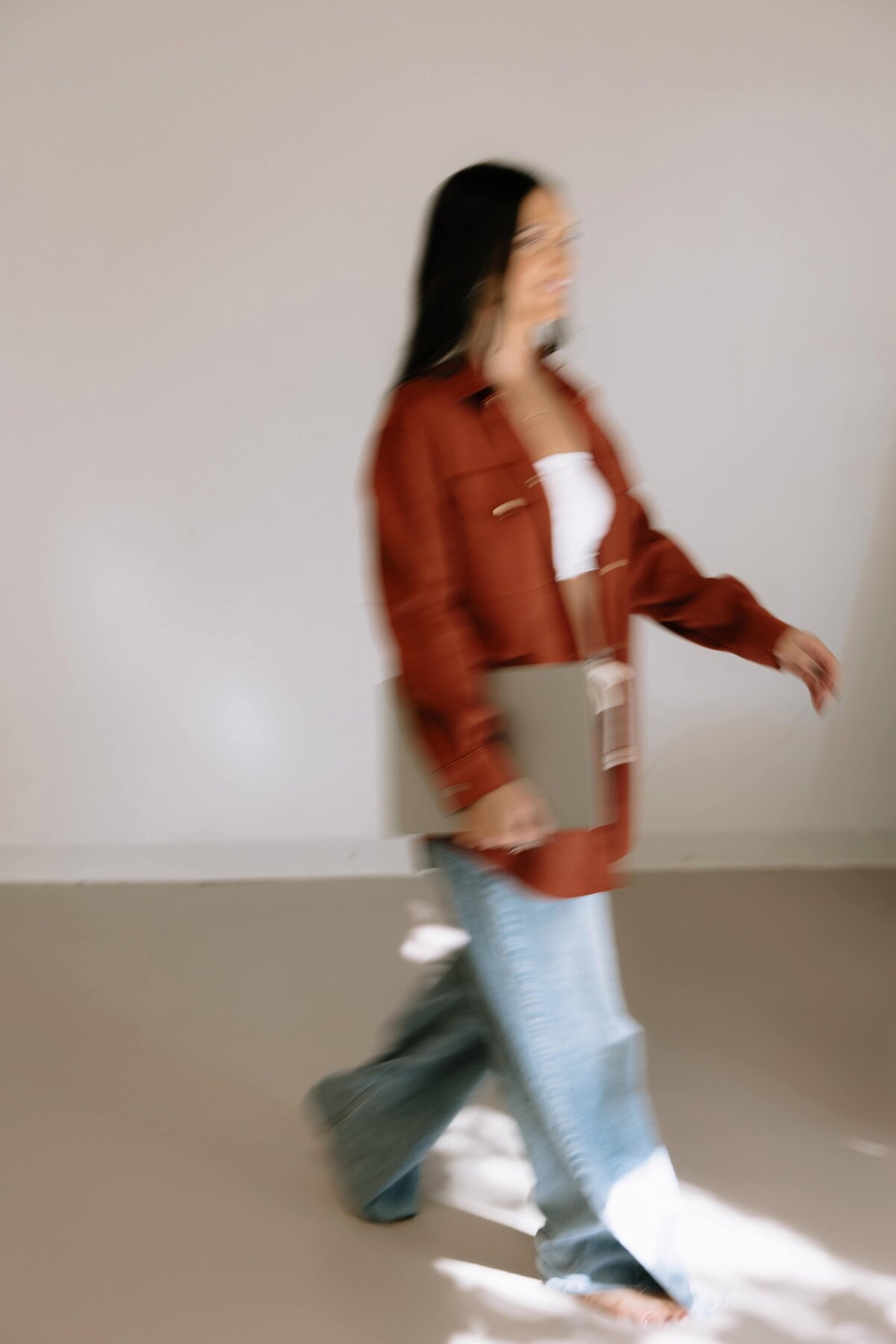 A blurry photo of a woman walking, holding her laptop. 