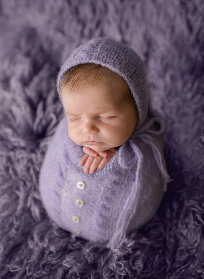 A cute baby posed in a purple wrap on a purple rug. Photo by Diane Owen Photography.