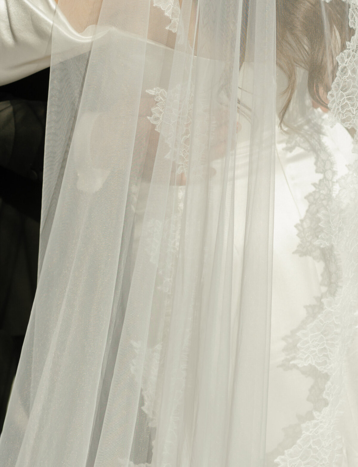 soft detail of groom embracing bride through long lace veil