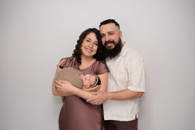 Parents smiling together while holding their newborn during Houston family portraits.