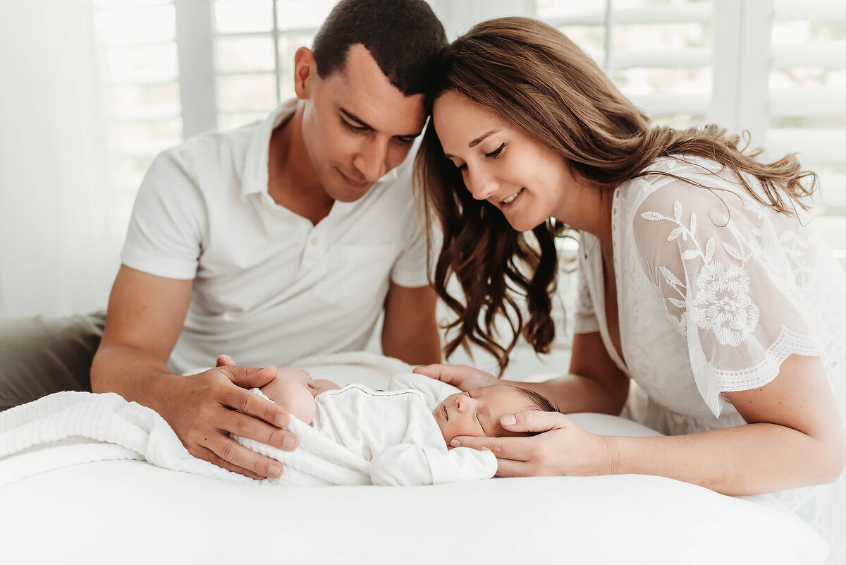 newborn on bed with parents looking down in Denver photo studio