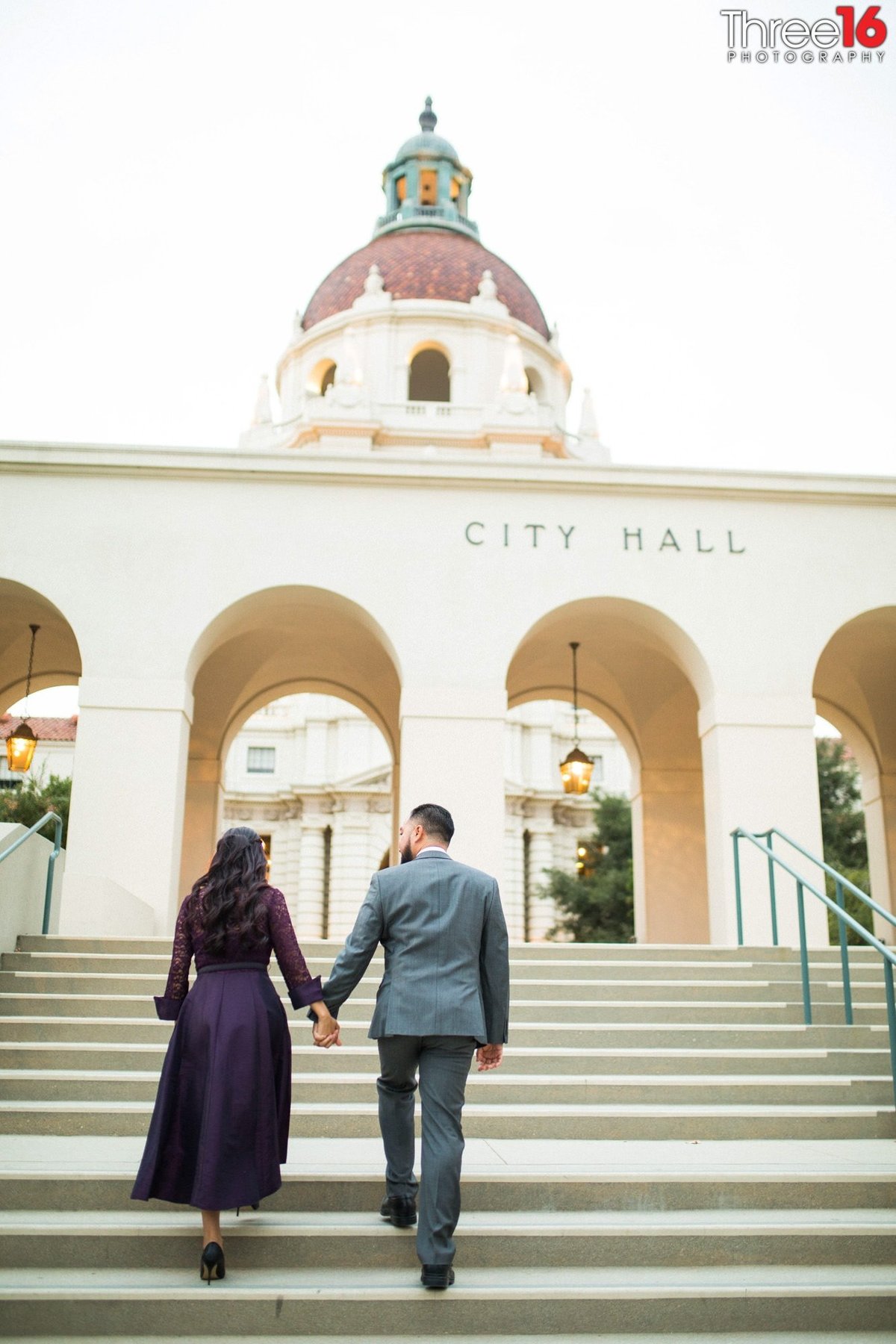 Engaged couple walk up the Pasadena City Hall steps holding hands