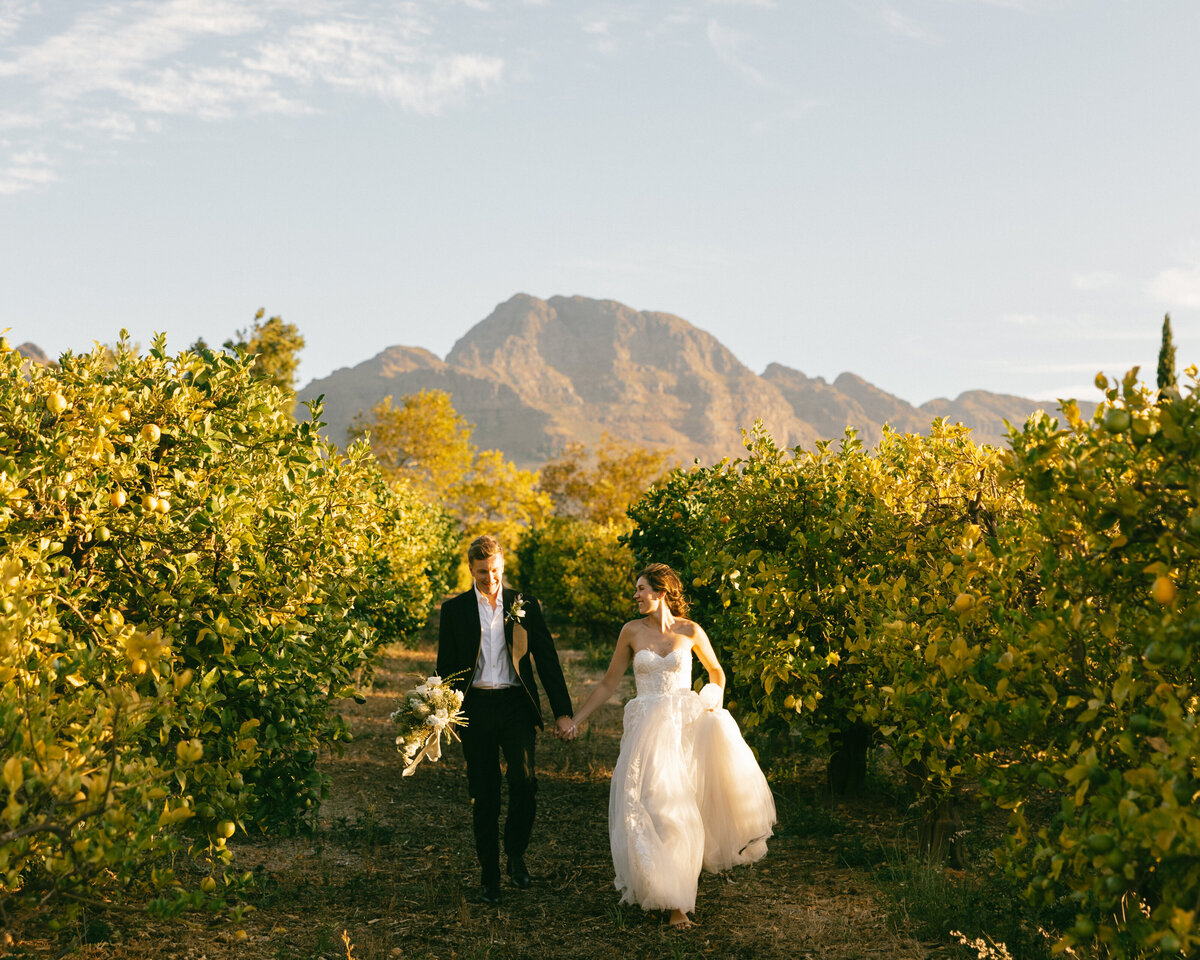 Bride and groom standing at an ivy covered alter laughing as groom puts wedding band on bride's finger