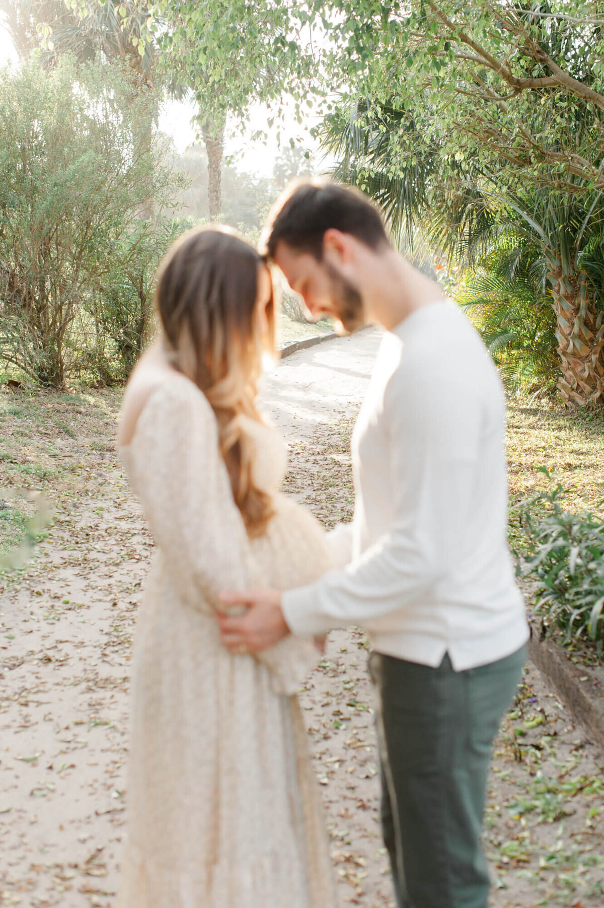 Couple is blurred while the stunning background is in focus of mom and dad holding moms belly on this beautiful greenery path