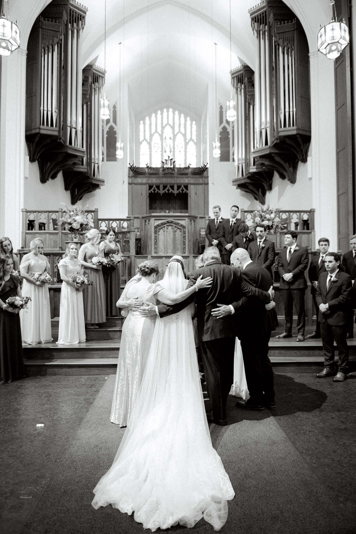 Black and white image of bride and groom's families praying at wedding ceremony in Fort Worth