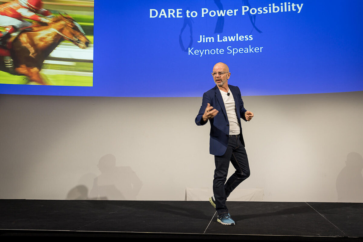 Professional headshot style of corporate speaker presenting under large screen with slides during event new york city.