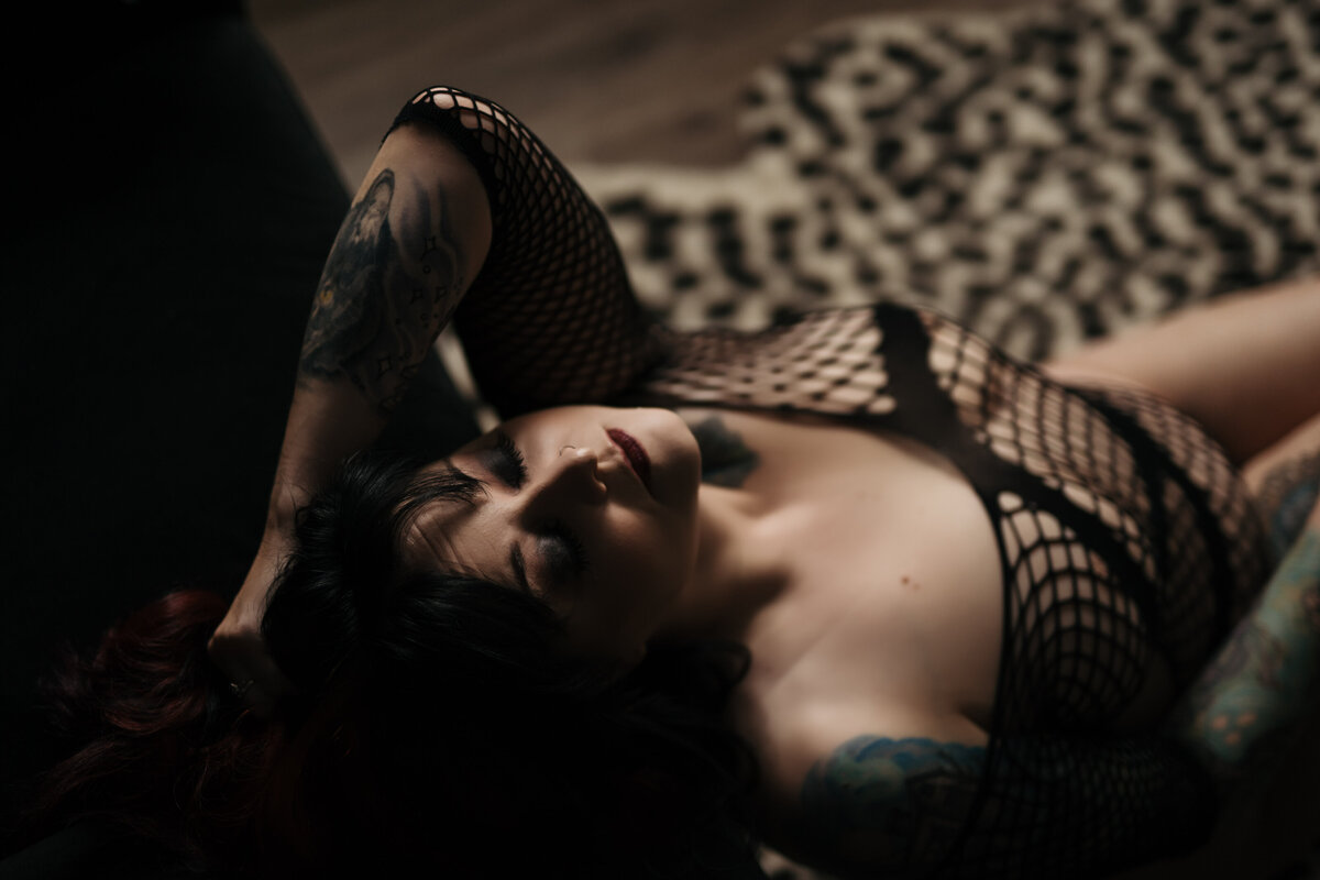 A woman in black mesh lingerie leans back on a couch while sitting on a cheetah print rug
