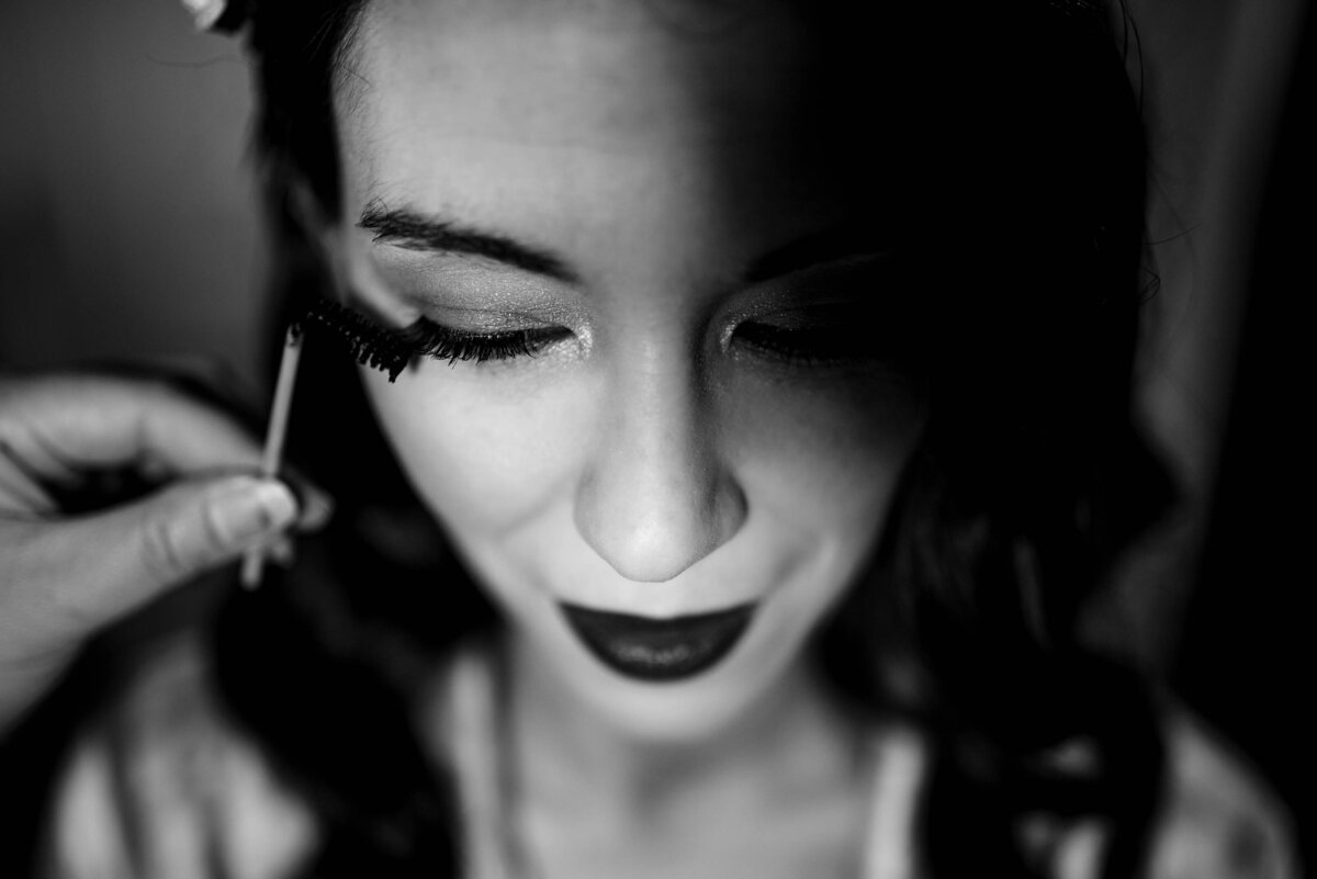 Black and white photograph top down and up close of bride having mascara applied by Charlotte wedding photographers DeLong Photography