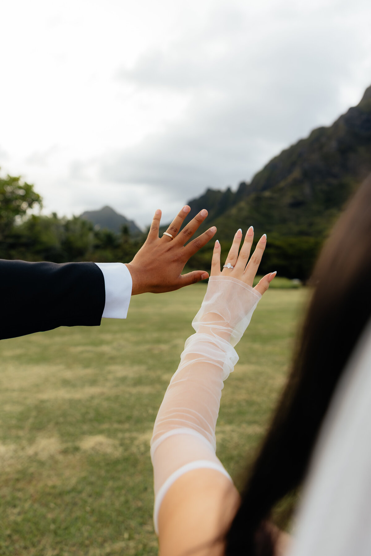 Close-up of bride and groom’s wedding rings with Hawaiian mountains in the background at Kualoa Regional Park