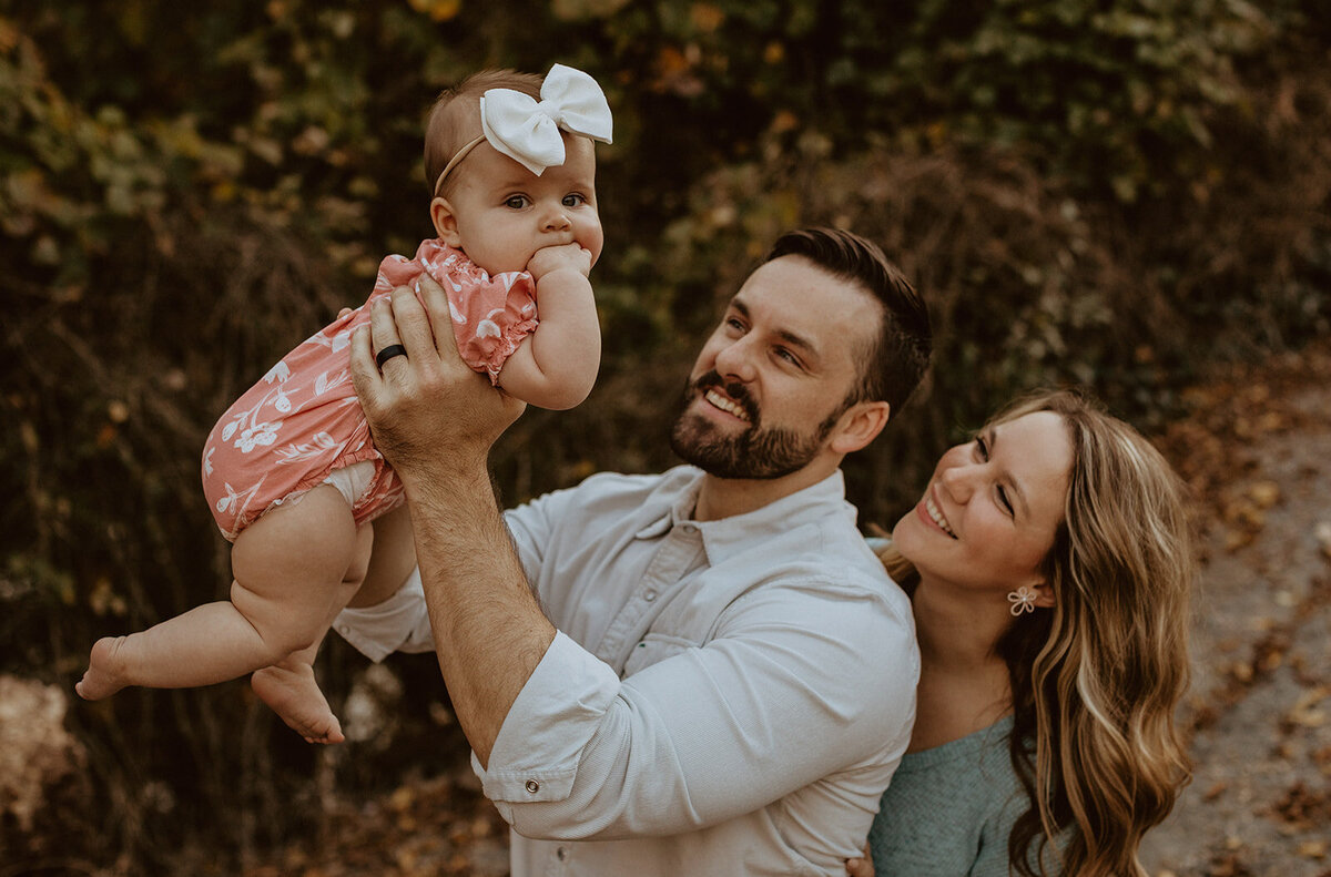 mom and dad hold daughter while she looks at the camera 