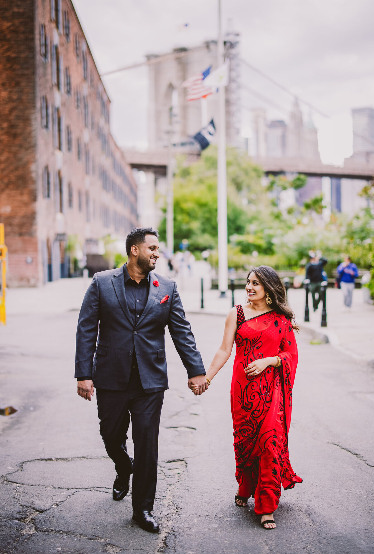 A bride in red indian sari walking with groom in a suit in dumbo brooklyn 
