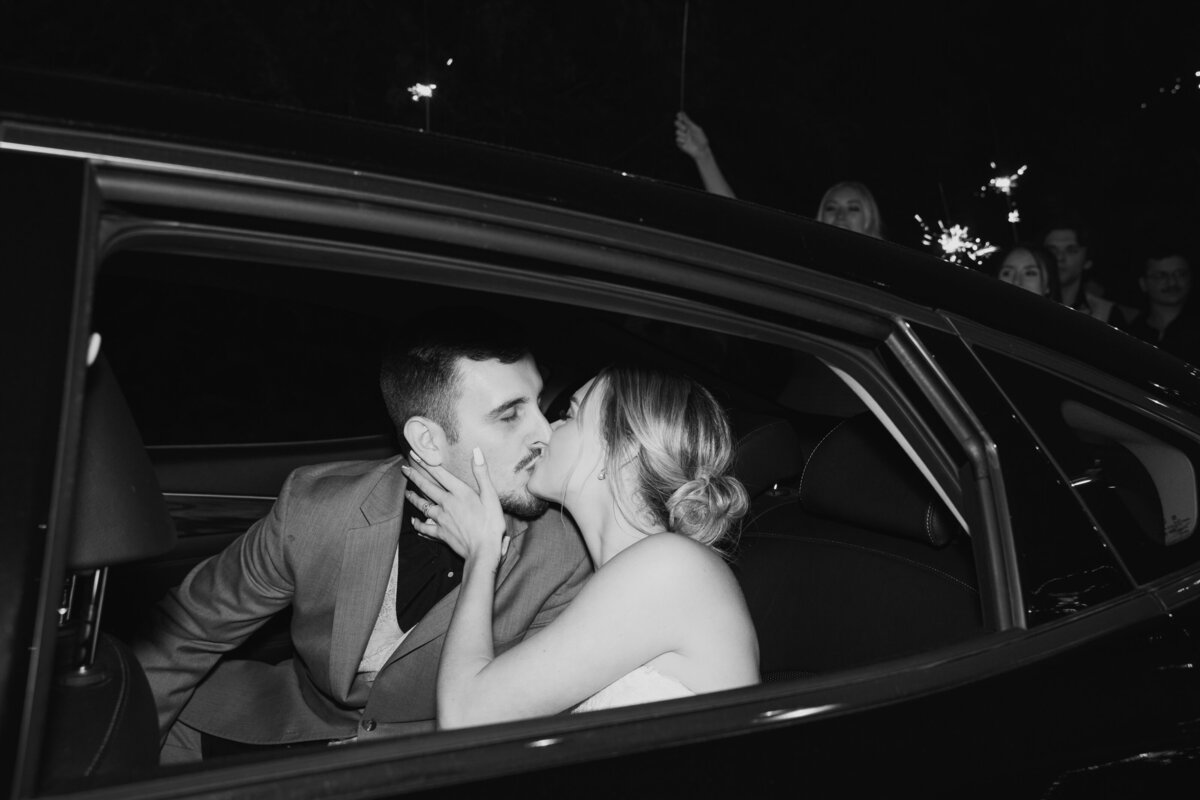 Bride and groom kissing inside of a black car