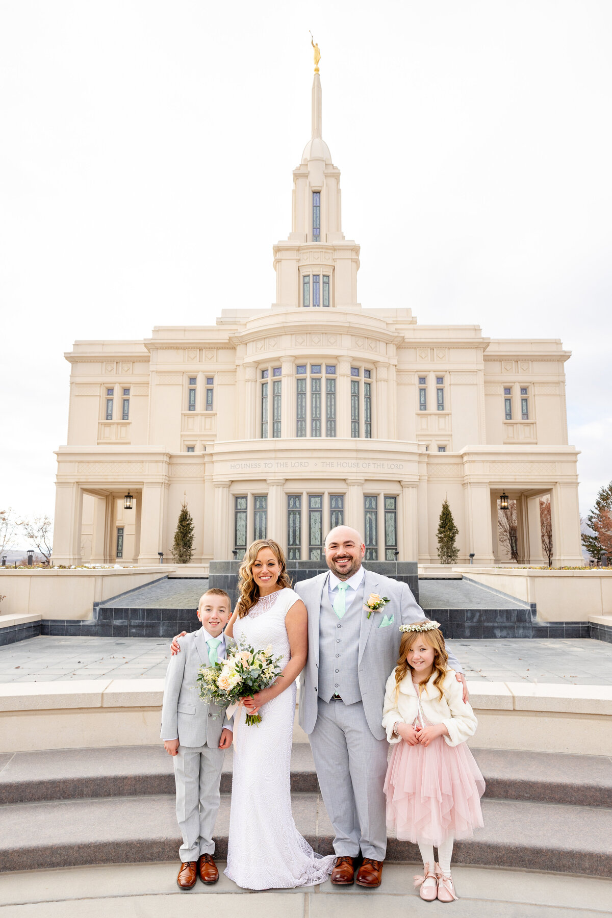 A newlywed couple poses with their children in front of the Payson Utah LDS Temple. The family is dressed in coordinating soft tones with the temple's elegant architecture as a backdrop.