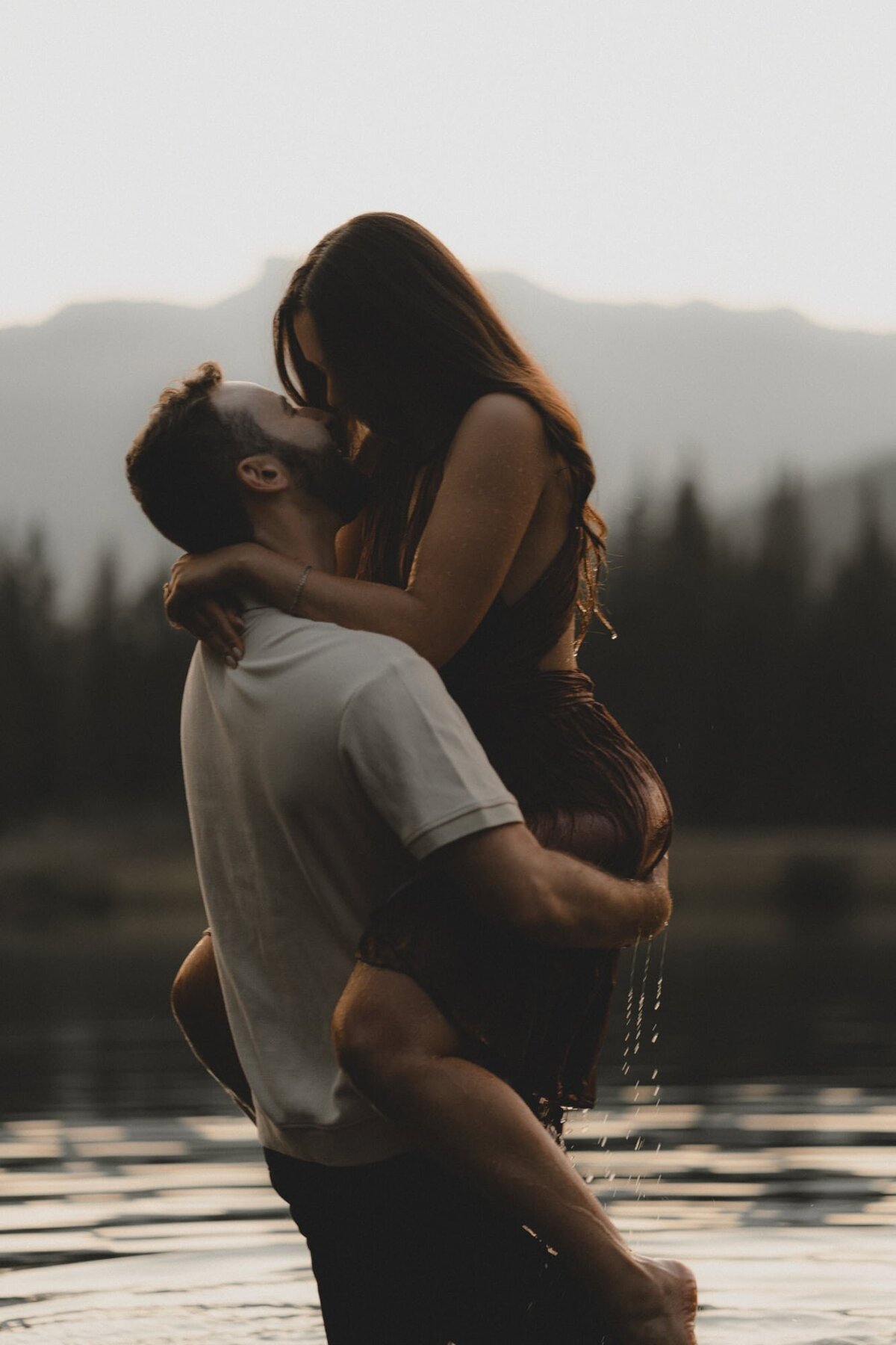 Engaged couple holding each other and kissing after getting in lake in Kananaskis