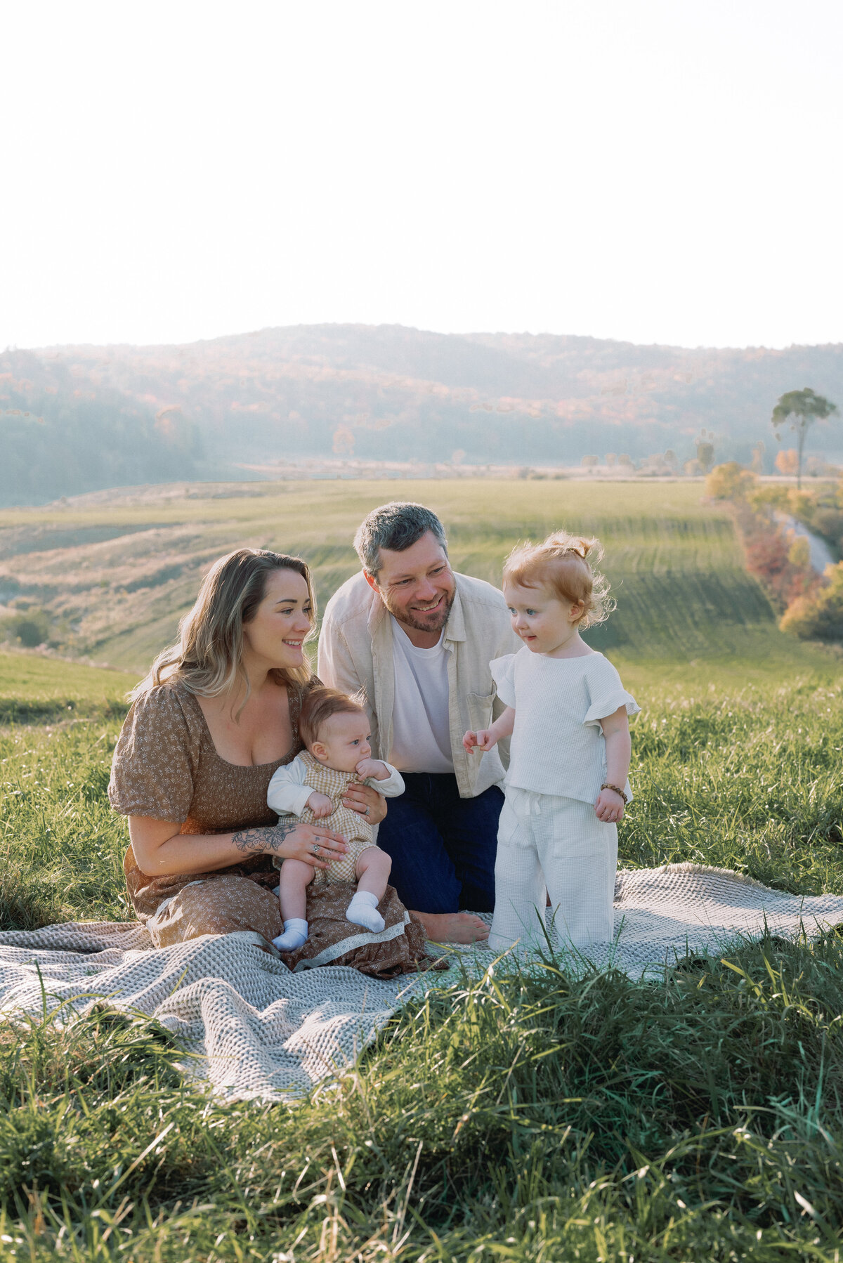Family of four sitting in a field with rolling hills in Ottawa