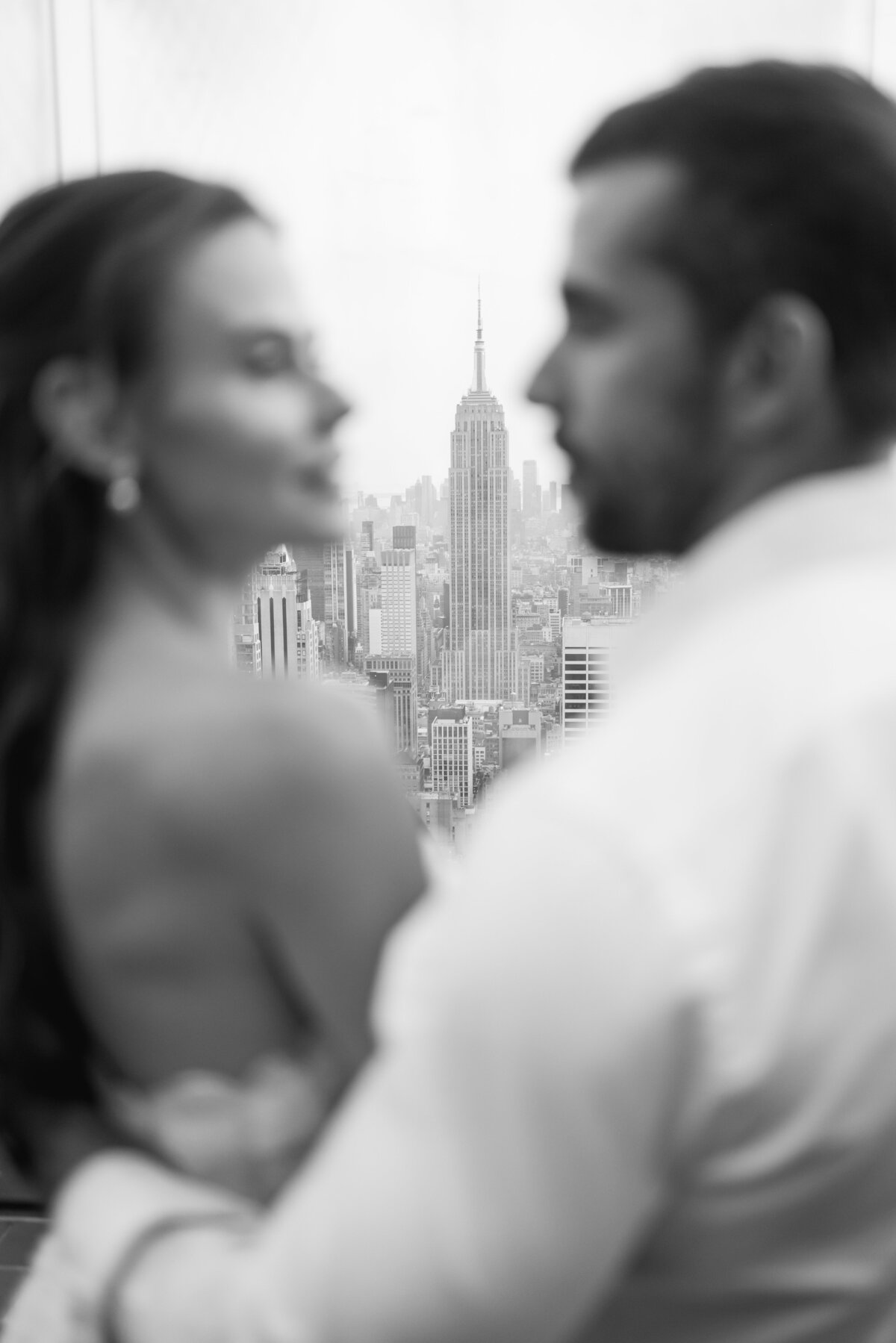 A fine art-inspired image of a bride and groom standing in serene elegance on Top of the Rock, bathed in soft light and surrounded by the beauty of New York City.