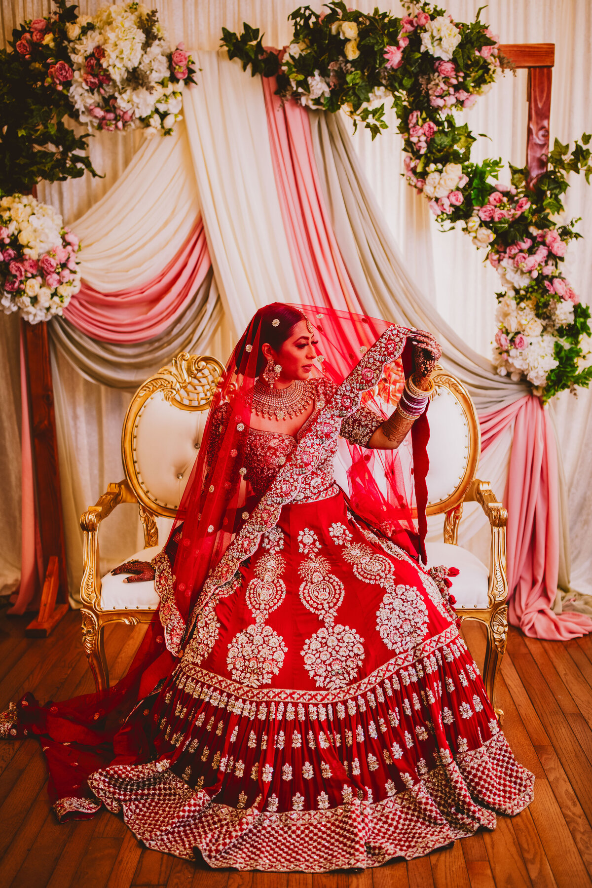 Sikh bride before the wedding taking a bridal portrait with the dupatta veil over her head in front of a floral backdrop