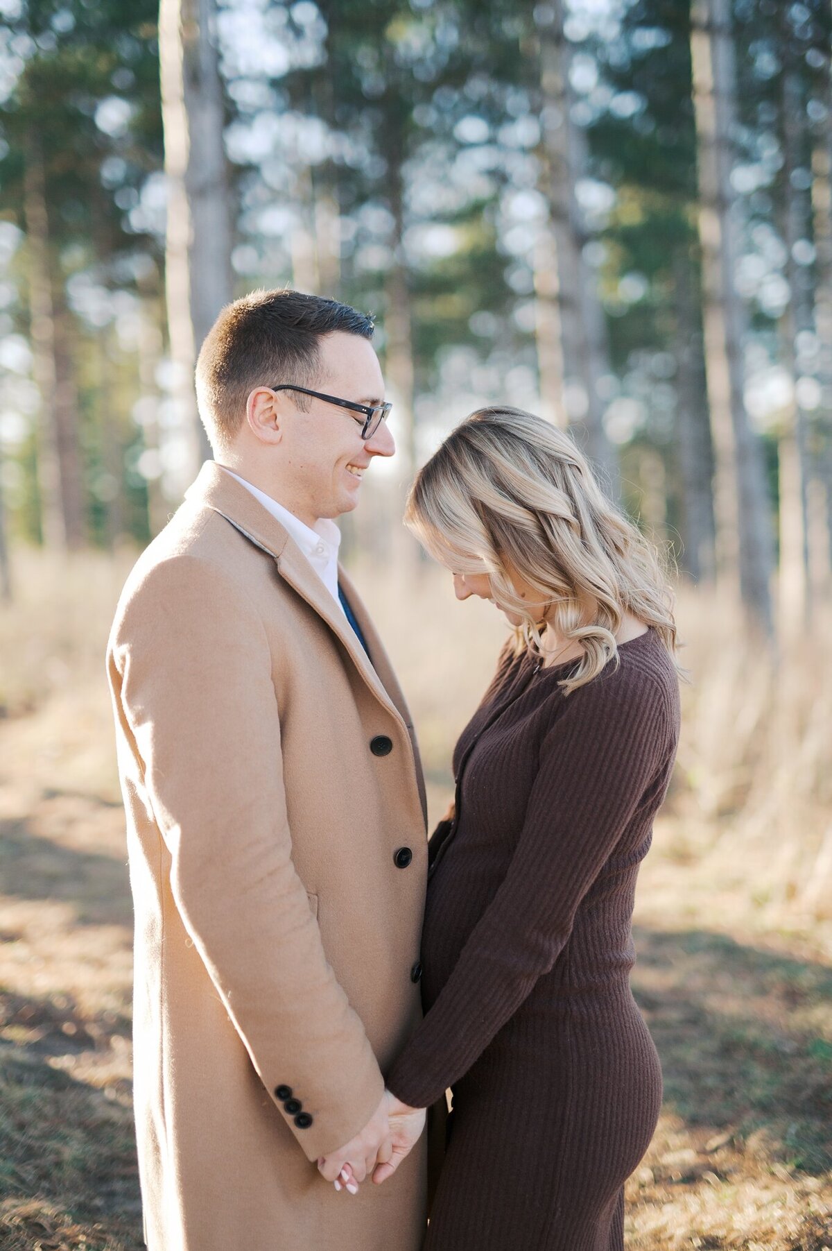Mom and dad-to-be smiling toward one another holding hands