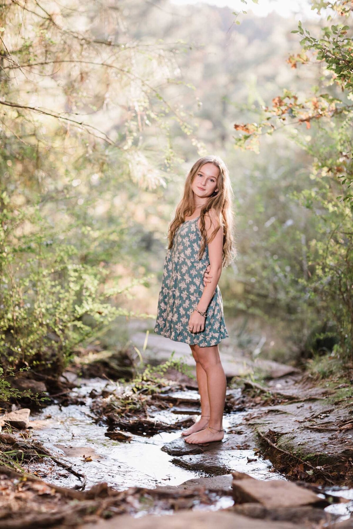 Senior portrait of a girl in a blue dress standing in a babbling brook.