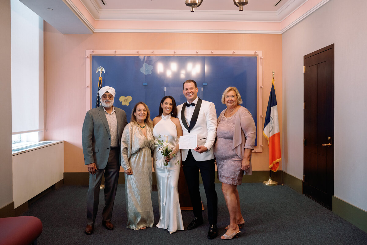 Bride Japna and groom Chris pose with family after their City Hall wedding ceremony, holding the marriage license and smiling together.