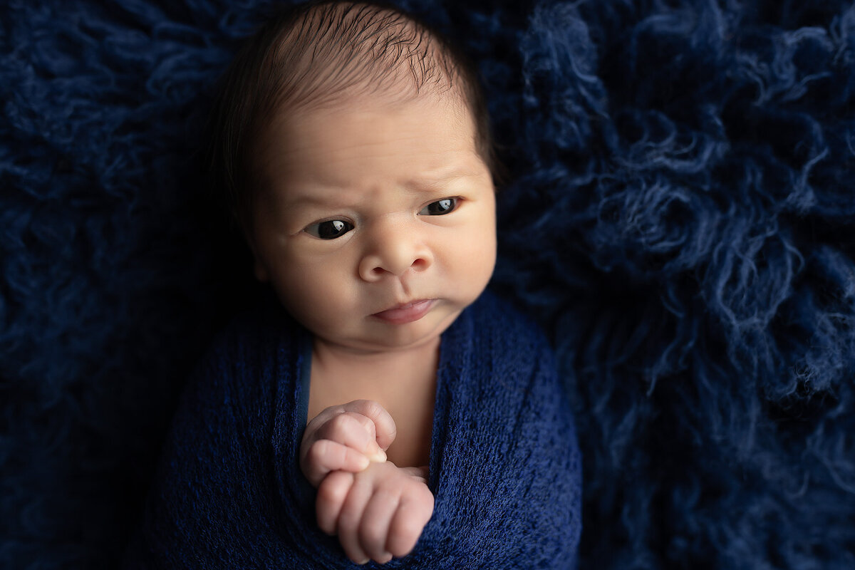 Close-up of baby wrapped in navy blue on fluffy fabric, captured by newborn photographer in Dallas.