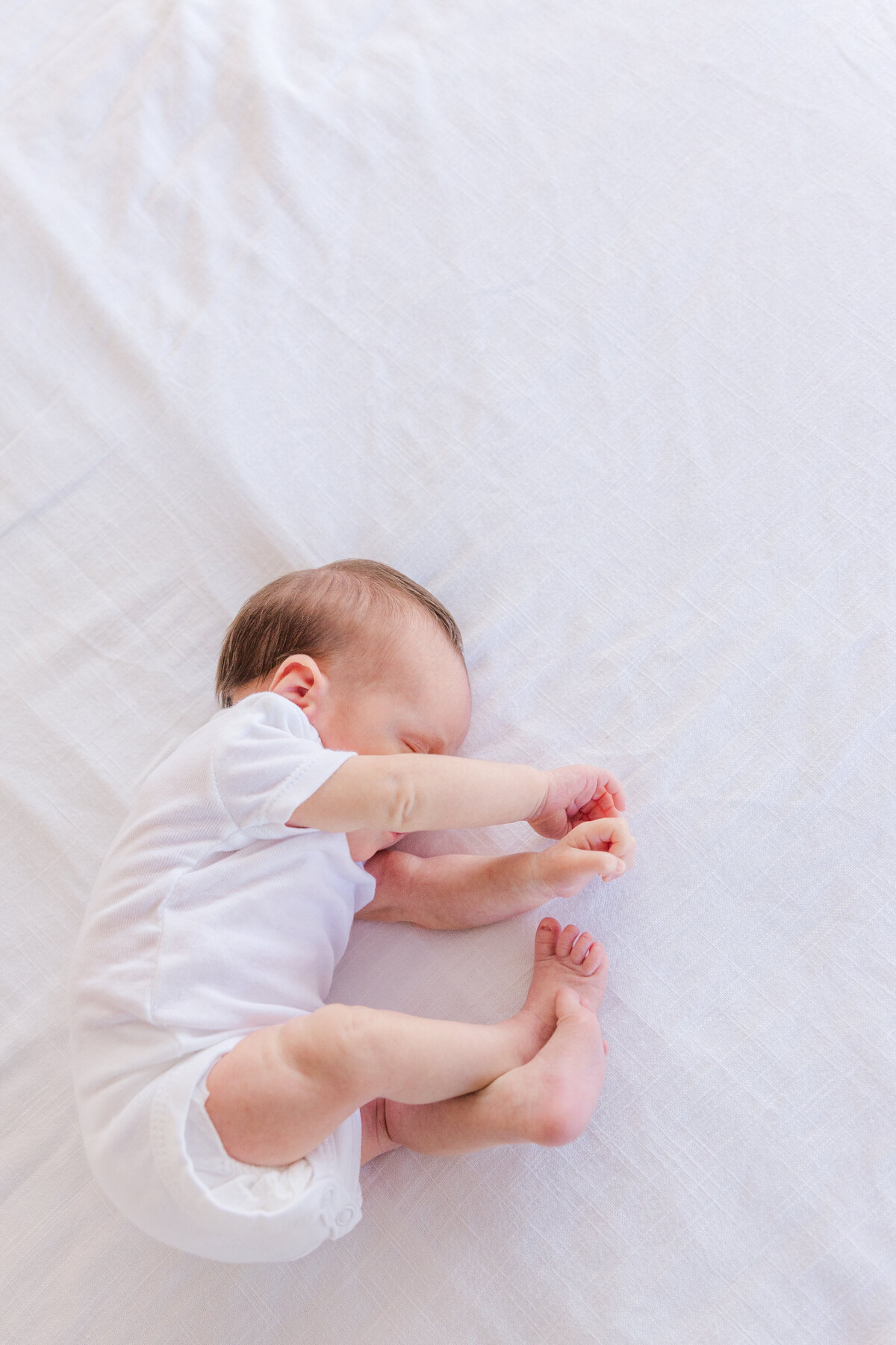 newborn in a white onsie sprawls out on a white  blanket