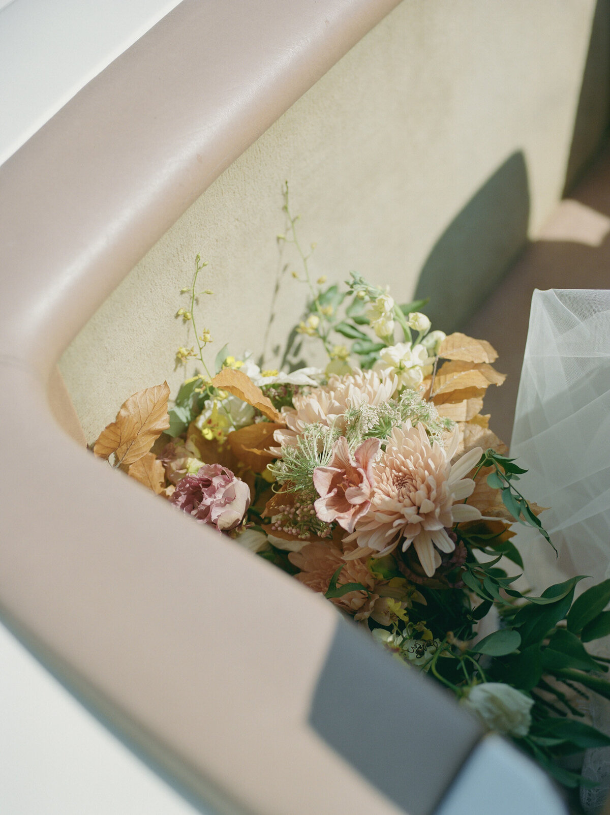 A soft, fall wedding bridal bouquet rests in the back of a vintage convertible wedding car in Detroit