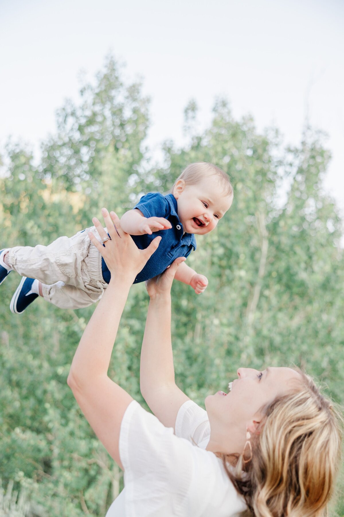 A smiling mom is swinging her baby above her head as he giggles captured by a Breckenridge Family Photographer