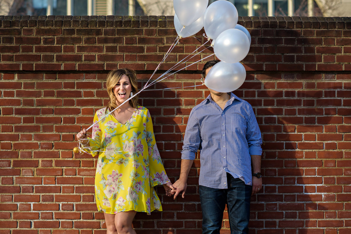 A pregnant mother holds balloons during a maternity session and the wind blows them in front of her husband's face.