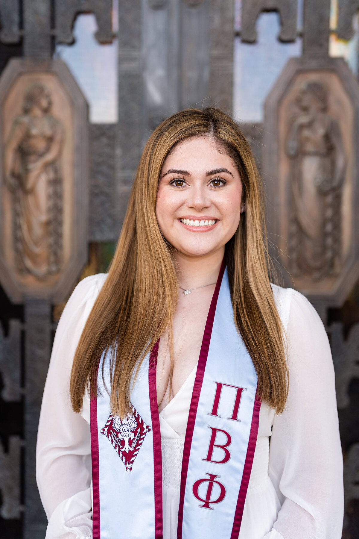 Texas A&M senior girl smiling and holding Pi Phi stole and white dress in front of Administration Building doors